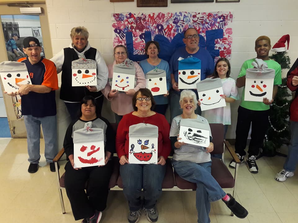 Group of people smiling and showing off their crafts that look like happy snowman faces.
