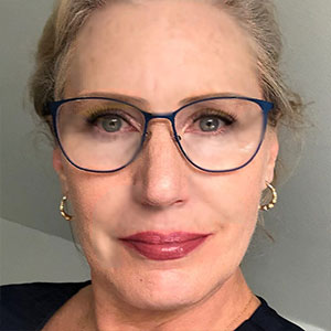 Profile photo of Mary Martin wearing blue rimmed glasses and gold earrings. She has blue eyes and blonde hair tied back.