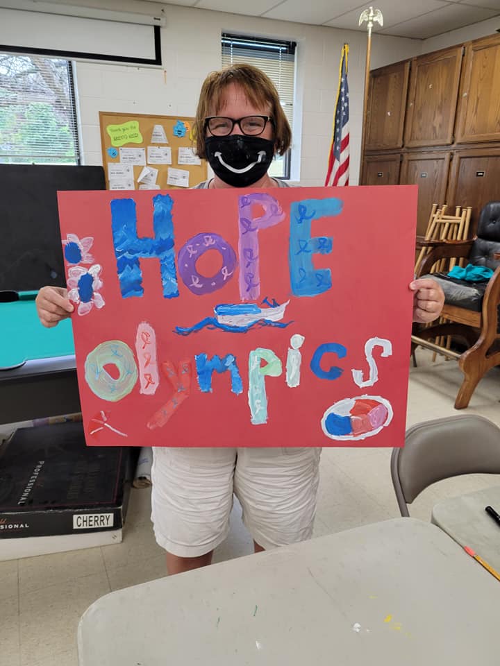 Photo of person with glasses holding a painted colorful sign that says Hope olympics.