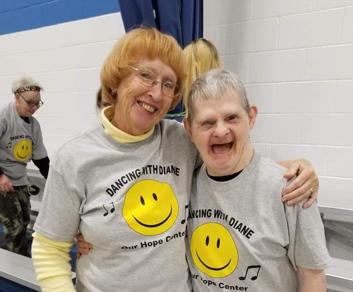 Two people standing in a gym smiling at the camera and wearing Dancing with Diane T-shirts.