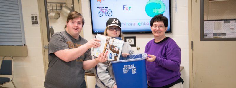 Photo of three people recycling and smiling at the camera.